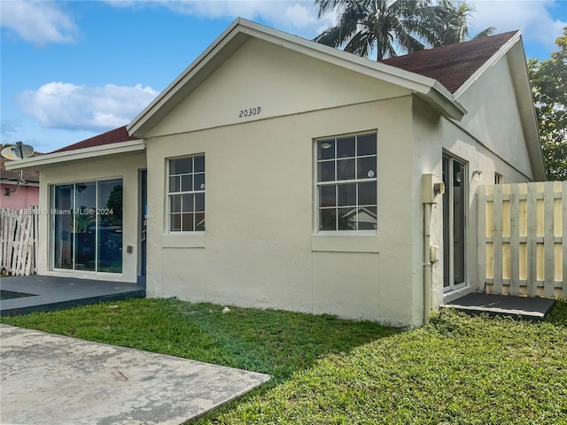 view of side of property with a patio area, a yard, fence, and stucco siding