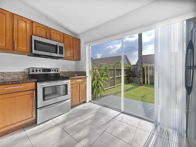 kitchen featuring appliances with stainless steel finishes, lofted ceiling, light tile patterned flooring, and dark stone counters