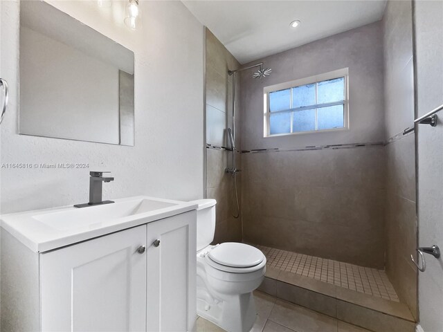 bathroom with toilet, a tile shower, vanity, and tile patterned floors