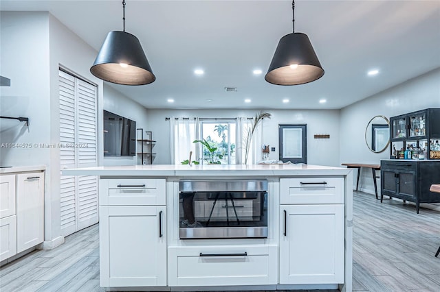 kitchen with light wood-type flooring, hanging light fixtures, white cabinetry, and stainless steel oven