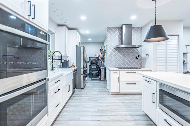 kitchen with backsplash, stainless steel appliances, wall chimney exhaust hood, washing machine and clothes dryer, and light stone countertops