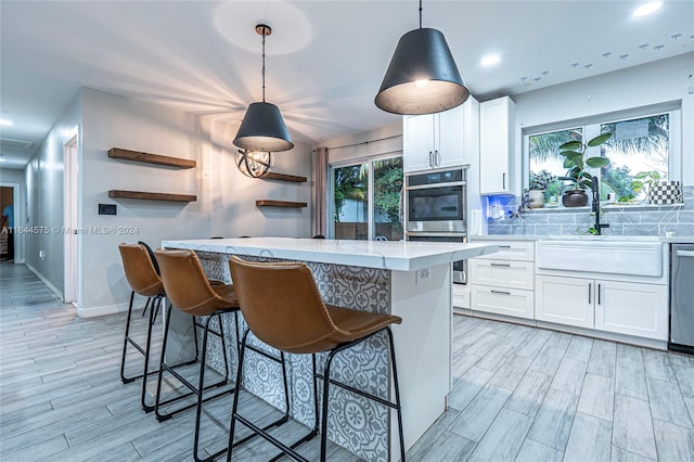 kitchen with stainless steel appliances, decorative backsplash, white cabinets, a kitchen breakfast bar, and hanging light fixtures