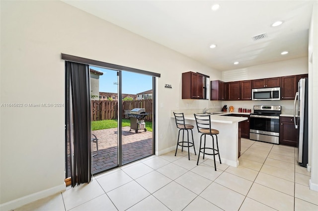 kitchen with a kitchen breakfast bar, light tile patterned flooring, kitchen peninsula, and stainless steel appliances