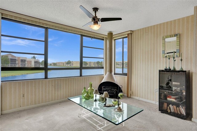 sunroom / solarium featuring a wood stove, ceiling fan, and a water view