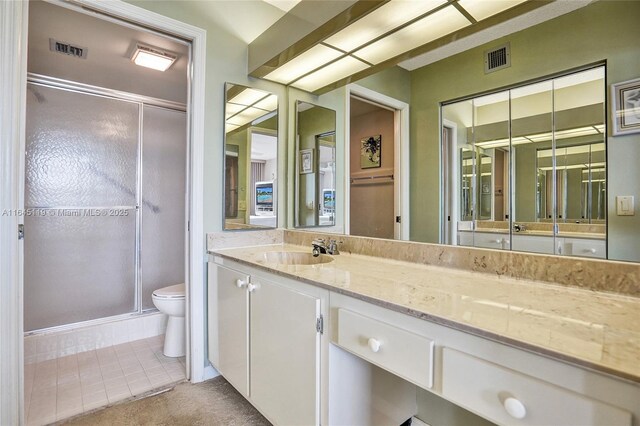 bathroom featuring tile patterned floors, vanity, a shower with shower door, and toilet