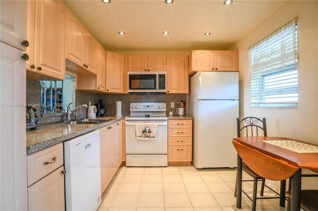 kitchen with sink, dark stone countertops, white appliances, light brown cabinetry, and light tile patterned floors