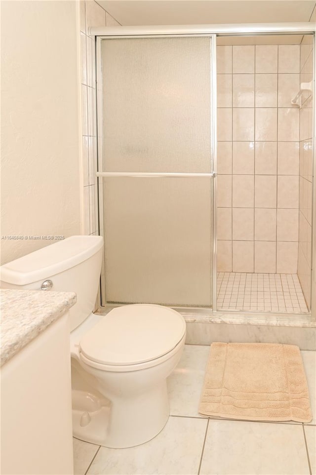 bathroom featuring tile patterned flooring, vanity, toilet, and a shower with door