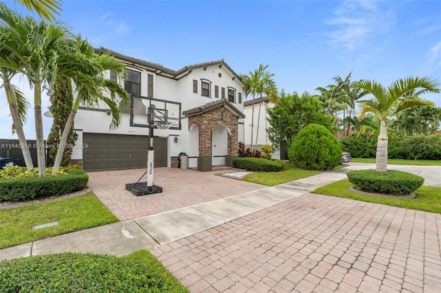 mediterranean / spanish-style home with a garage, stone siding, decorative driveway, and stucco siding