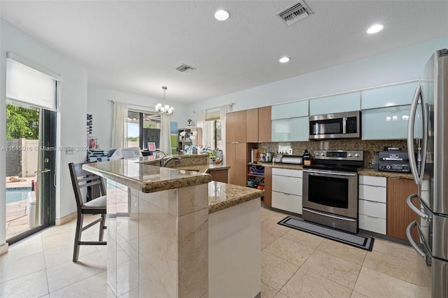 kitchen featuring appliances with stainless steel finishes, stone countertops, light tile patterned floors, a kitchen breakfast bar, and a notable chandelier