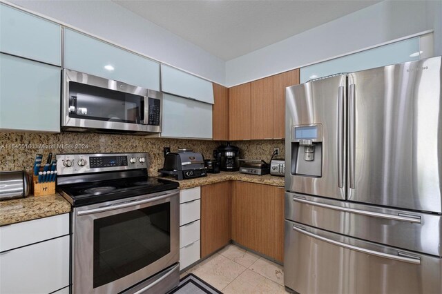 kitchen featuring backsplash, appliances with stainless steel finishes, light tile patterned flooring, and light stone countertops