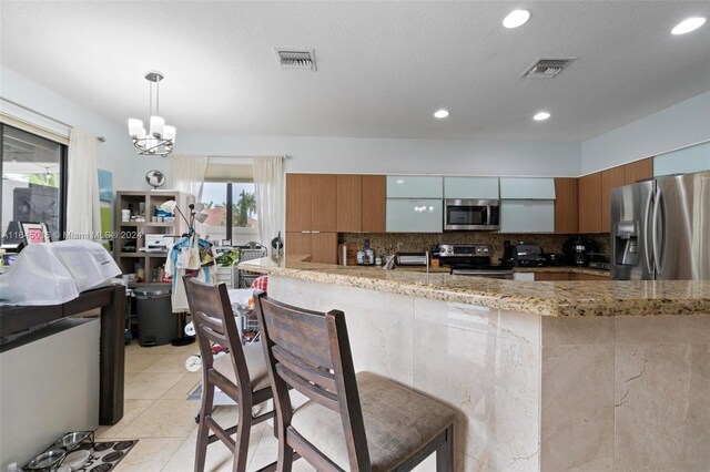 kitchen with decorative backsplash, light stone countertops, light tile patterned floors, decorative light fixtures, and stainless steel appliances