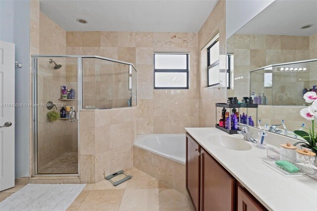 bathroom with tile patterned flooring, independent shower and bath, vanity, and tile walls