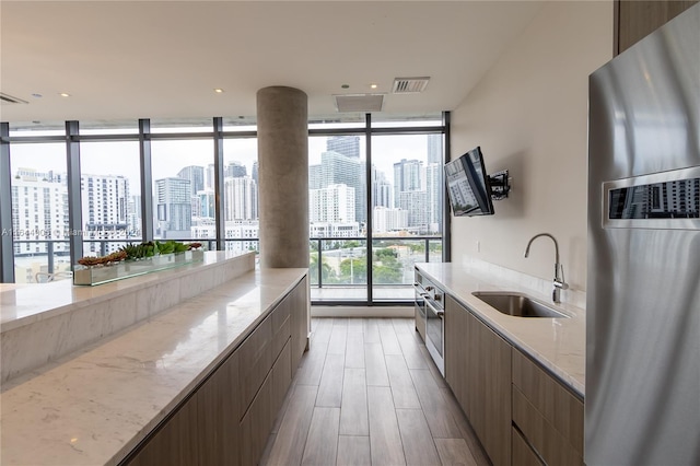 kitchen with sink, stainless steel fridge with ice dispenser, light wood-type flooring, and expansive windows