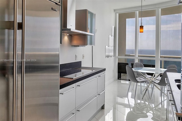 kitchen with wall chimney range hood, black electric cooktop, light tile patterned flooring, white cabinetry, and stainless steel refrigerator