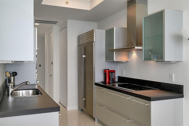 kitchen featuring black electric stovetop, wall chimney range hood, built in refrigerator, sink, and light tile patterned flooring