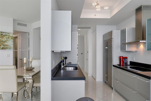 kitchen with black electric stovetop, gray cabinetry, wall chimney range hood, sink, and stainless steel built in refrigerator