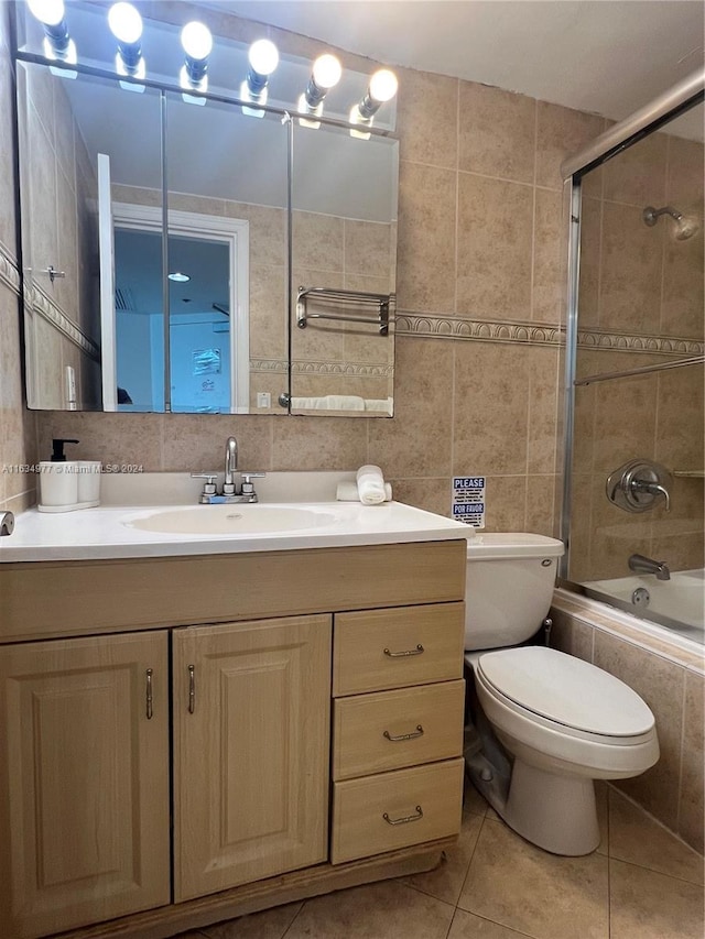 bathroom with tile patterned floors, vanity, toilet, tiled shower / bath, and tile walls