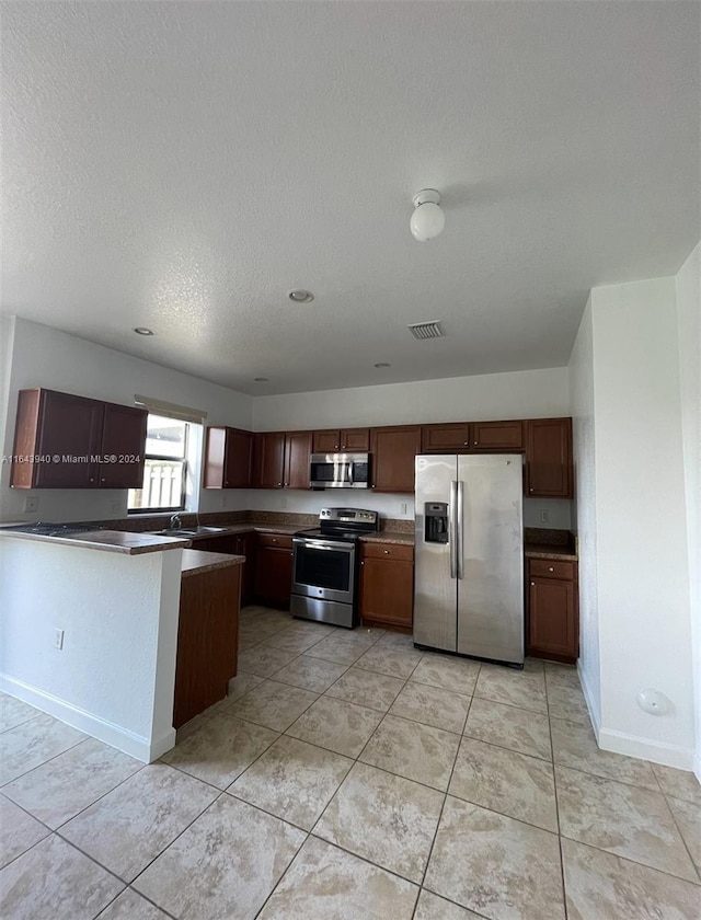 kitchen with a textured ceiling, kitchen peninsula, light tile patterned floors, and appliances with stainless steel finishes