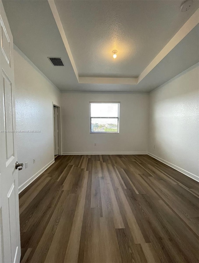 unfurnished room featuring a tray ceiling, dark wood-type flooring, and a textured ceiling