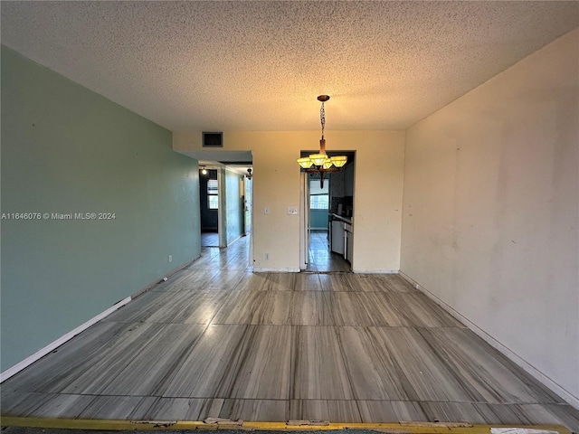 unfurnished dining area featuring tile patterned floors, a textured ceiling, and an inviting chandelier