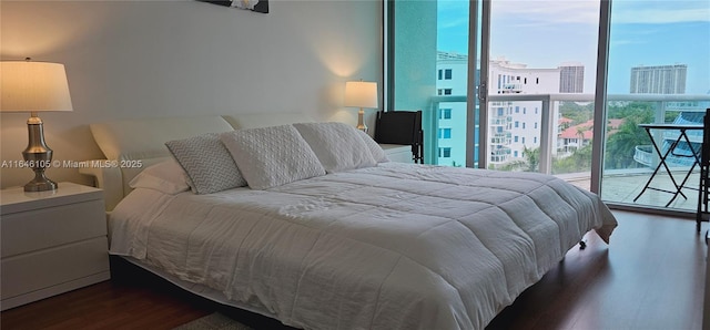 bedroom with a view of city, expansive windows, and wood finished floors