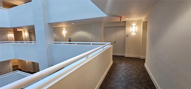 hall with dark carpet, a towering ceiling, an upstairs landing, and baseboards