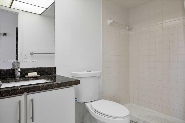 bathroom with toilet, a tile shower, and vanity