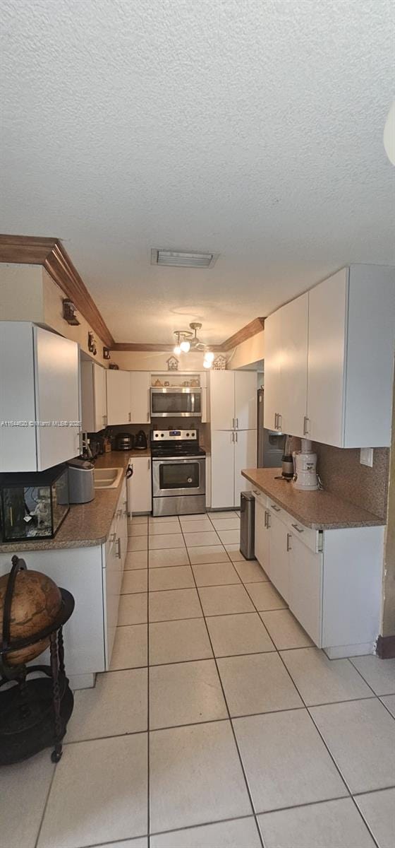 kitchen featuring appliances with stainless steel finishes, sink, white cabinets, light tile patterned floors, and a textured ceiling