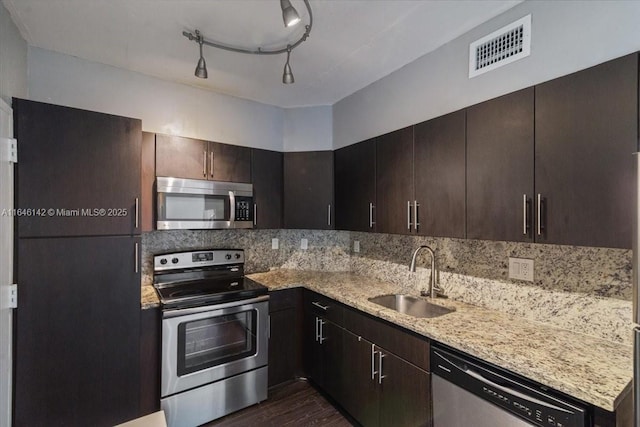 kitchen with sink, rail lighting, tasteful backsplash, light stone counters, and appliances with stainless steel finishes