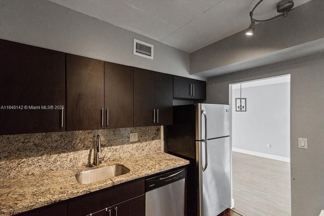 kitchen featuring decorative backsplash, appliances with stainless steel finishes, light stone countertops, dark brown cabinetry, and sink