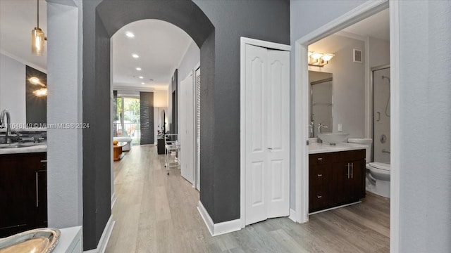 hallway featuring sink, crown molding, and light wood-type flooring