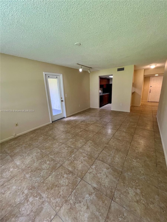 empty room featuring visible vents, baseboards, a textured ceiling, and rail lighting