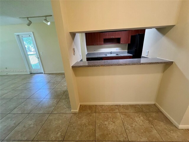 kitchen featuring rail lighting, sink, black refrigerator, light tile patterned floors, and kitchen peninsula