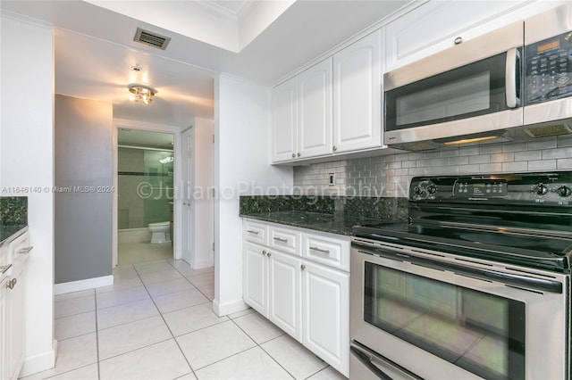 kitchen featuring dark stone countertops, white cabinetry, appliances with stainless steel finishes, light tile patterned floors, and backsplash