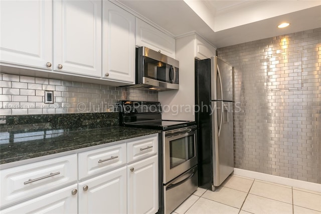 kitchen with dark stone counters, decorative backsplash, white cabinets, appliances with stainless steel finishes, and light tile patterned floors