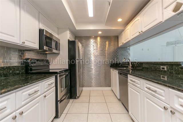 kitchen with light tile patterned floors, backsplash, white cabinetry, appliances with stainless steel finishes, and dark stone counters