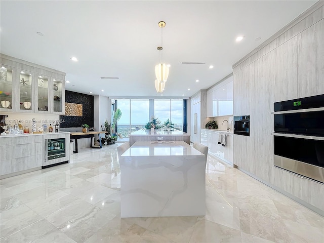 kitchen with beverage cooler, hanging light fixtures, a spacious island, double oven, and sink