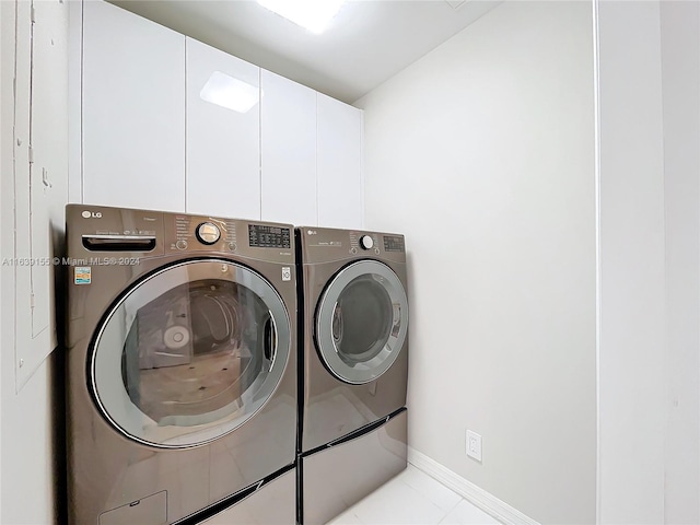 clothes washing area featuring light tile patterned flooring, washing machine and dryer, and cabinets