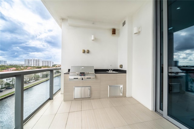 balcony featuring an outdoor kitchen, grilling area, a water view, a city view, and a sink