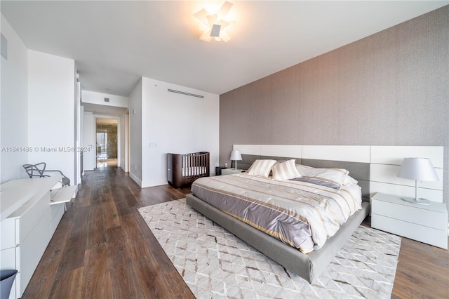 bedroom featuring an accent wall, wallpapered walls, baseboards, and wood finished floors