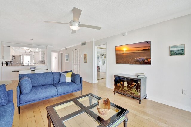 living room featuring a textured ceiling, light hardwood / wood-style flooring, ceiling fan with notable chandelier, and ornamental molding