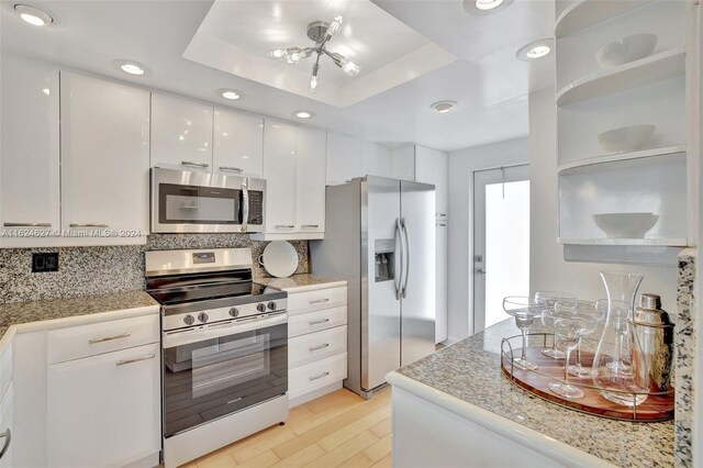 kitchen featuring appliances with stainless steel finishes, light hardwood / wood-style flooring, decorative backsplash, white cabinets, and a tray ceiling