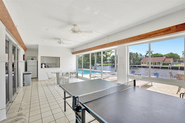 rec room with ceiling fan, light tile patterned floors, and a water view