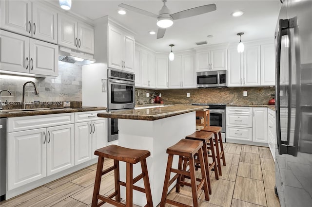 kitchen featuring a kitchen island, hanging light fixtures, stainless steel appliances, ceiling fan, and white cabinets