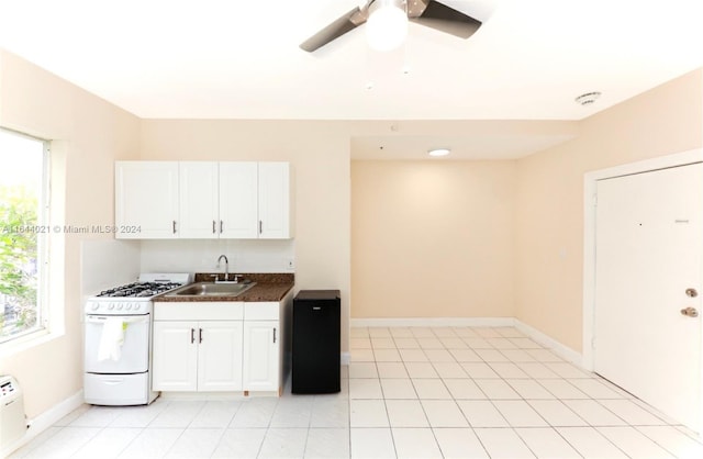 kitchen featuring white range with gas cooktop, sink, white cabinets, light tile patterned floors, and ceiling fan