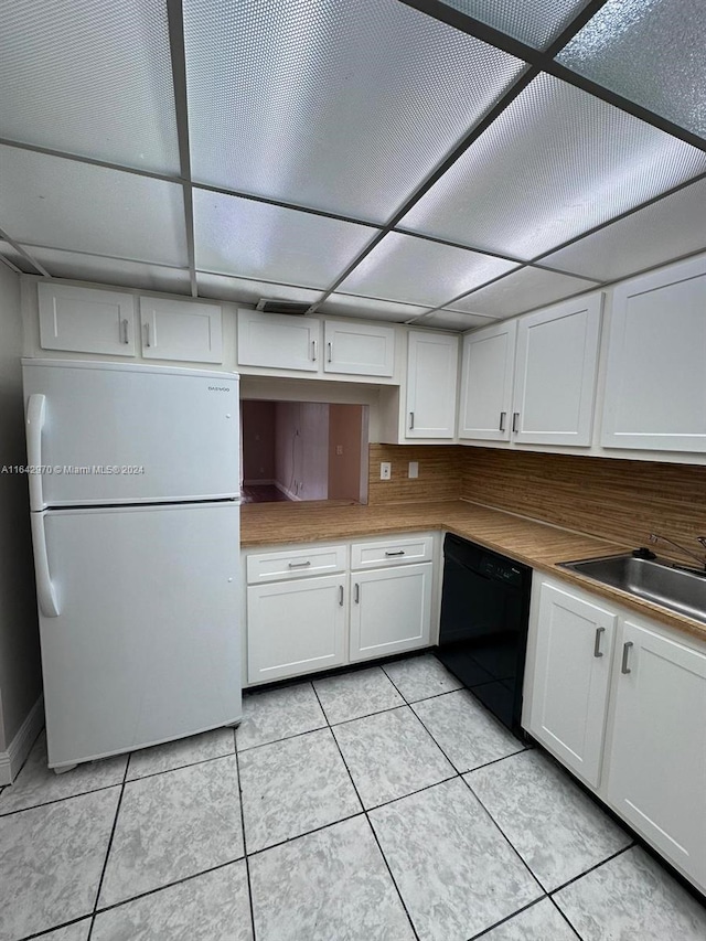 kitchen featuring a sink, light tile patterned flooring, white cabinets, black dishwasher, and freestanding refrigerator
