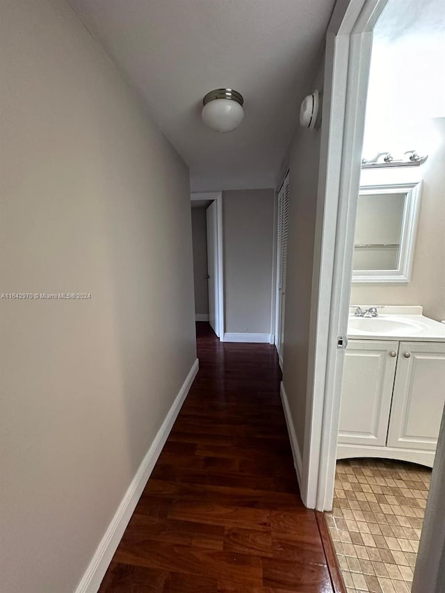 hallway featuring baseboards, wood finished floors, and a sink