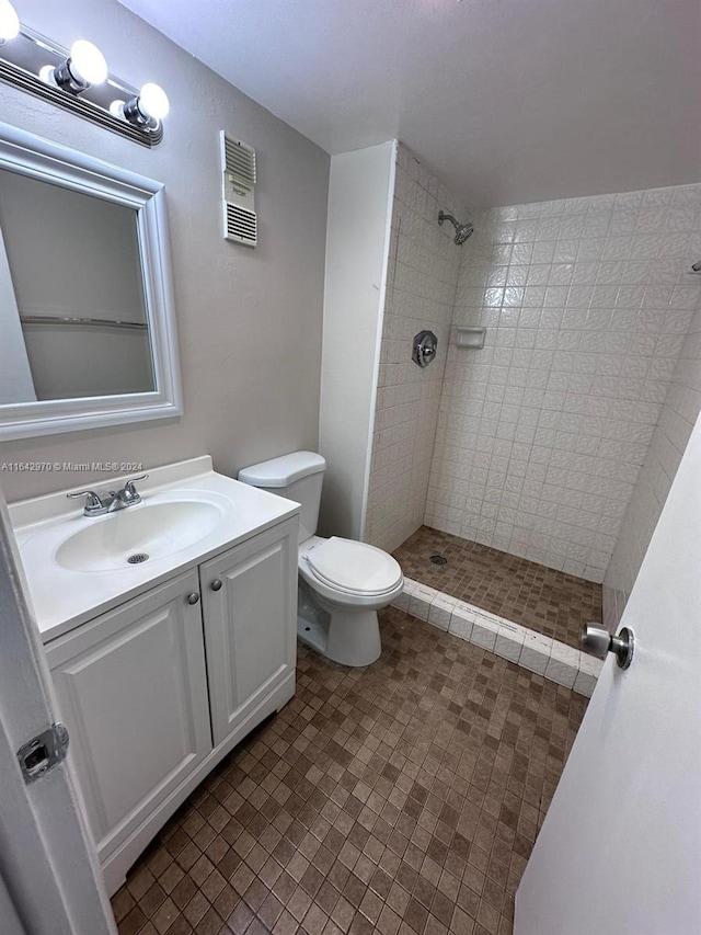 bathroom with tile patterned floors, vanity, tiled shower, and toilet