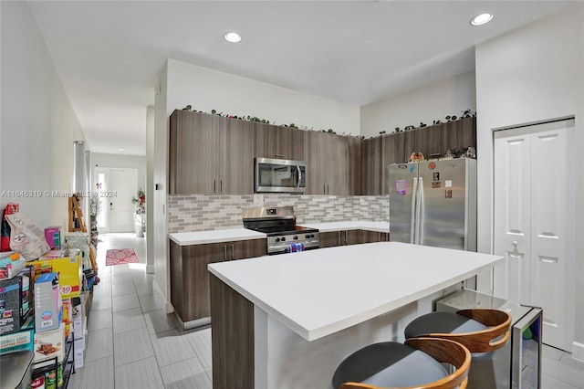 kitchen with a center island, stainless steel appliances, light tile patterned flooring, a kitchen breakfast bar, and tasteful backsplash