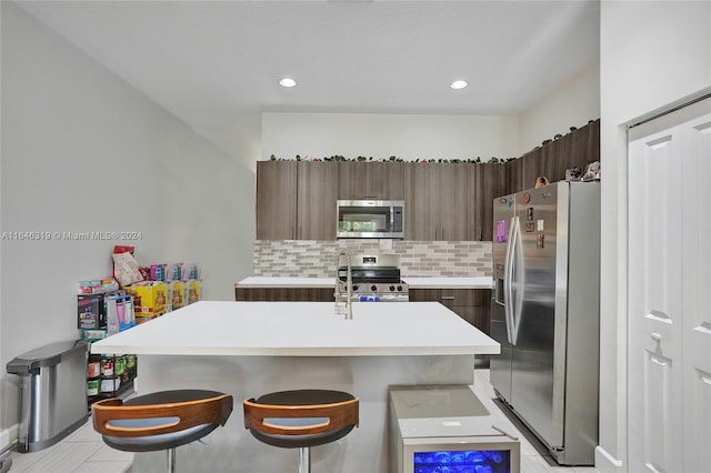 kitchen with backsplash, light tile patterned floors, stainless steel appliances, an island with sink, and a kitchen breakfast bar